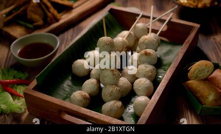 3/4-Schuss thailändisches traditionelles Straßenessen mit gegrillten Fleischbällchen und gebratenen Frühlingsrollen auf Holztisch Stockfoto