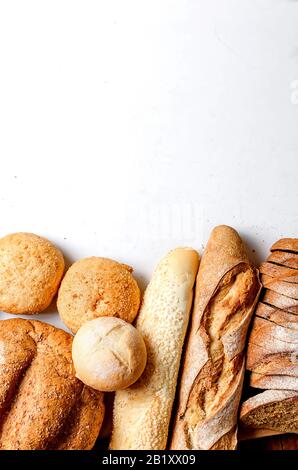 Auswahl an frisch gebackenem Brot mit Weizenköpfen auf weißem Tisch, Foto mit niedrigem Schlüssel, Konzept für gesunde oder hausgemachte Speisen, für die Bäckerei Stockfoto