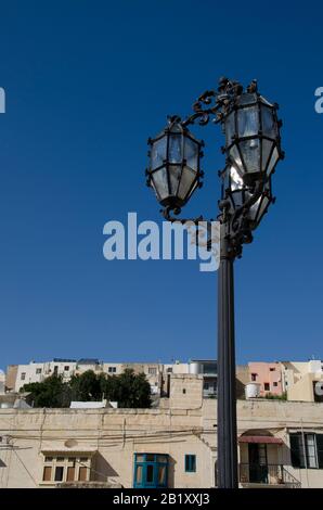 Elegante, schmiedeeiserne Straßenleuchte mit blauem Himmel und traditioneller maltesischer Architektur Stockfoto