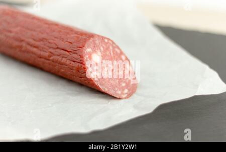 Traditioneller Salami. Ein in Papier gewickeltes Stück Salamiwurst auf einem Steinbrett. Stockfoto