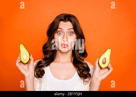 Nahaufnahme des fröhlichen positiven, hübschen, attraktiven Youngster mit Lippen, die zwei Hälften eines Avocado halten, damit Sie sich isoliert entscheiden können Stockfoto