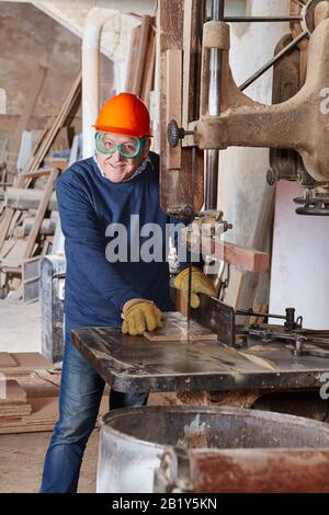 Der alte Zimmermann sägt Holz auf einer Bandsäge in einer Tischlerei Stockfoto