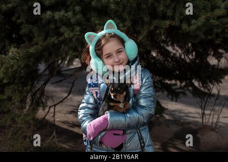 Ein wenig chihuahua legt sich in die Arme seines Besitzers. Schulkind im Winter Kleidung auf der Straße. Mädchen 9 Jahre alt. Stockfoto