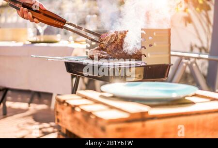 Küchenchef grillen T-Bone Steak beim Grillabendessen im Freien - Mann, der Fleisch für eine familiengrillmahlzeit im Garten im Hinterhof kocht - Samme Lifestyle, Essen und Stockfoto