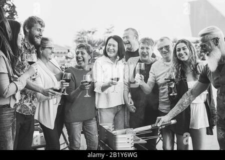 Fröhliche Familie, die beim Barbecue-Dinner im Freien Wein isst und trinkt - Multiracial reife und junge Leute, die Spaß am bbq-sonntagmenü haben - Essen und Sommer Stockfoto