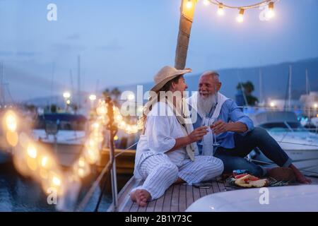 Älteres Paar jubelt während des Hochzeitstages mit Champagner auf einem segelboot - Alte Leute haben Spaß beim Trinken und Lachen - Joyfu Stockfoto