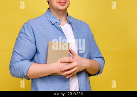Ein Mann in einem Hemd auf gelbem Hintergrund hält ein Buch. Nahaufnahme. Stockfoto