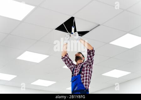 Volle Länge Portrait von Elektriker Trittleiter installiert Beleuchtung an der Decke im Büro Stockfoto