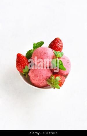 Erdbeereiskuppen mit frischen Erdbeeren in der Schüssel über weißem Steinhintergrund mit freiem Text. Leckeres kaltes Sommerdessert. Stockfoto