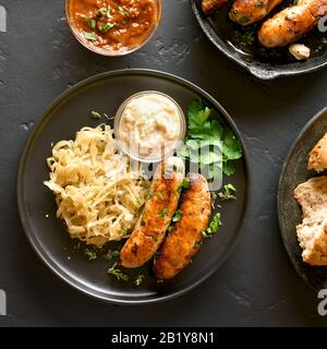 Gegrillte Würstchen mit Sauerkraut und Meerrettich auf die Platte über der schwarzen Stein Hintergrund. Ansicht von oben, flach Stockfoto