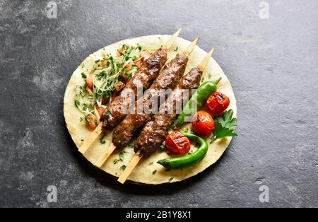 Türkische Adana Kebab mit frischem Gemüse auf Fladenbrot über schwarzem Steingrund. Nahansicht Stockfoto