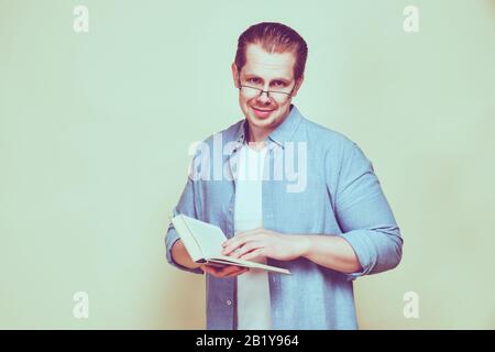 Ein Mann in einem Hemd liest ein Buch mit Brille und schaut auf die Kamera. Getont. Nahaufnahme. Stockfoto