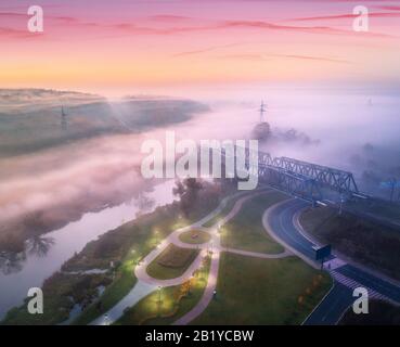 Luftbild des beeindruckenden Parks in der Nähe von Fluss- und Eisenbahnbrücke im Nebel Stockfoto