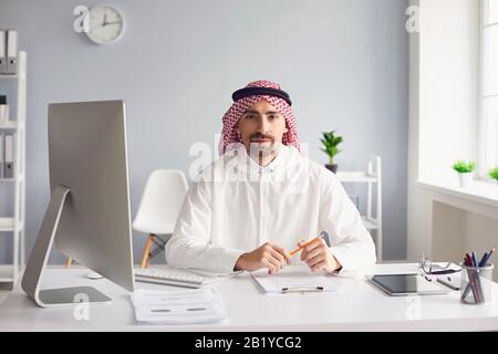 Ruhiger arabischer Mann sitzt an einem Tisch im Büro. A Stockfoto