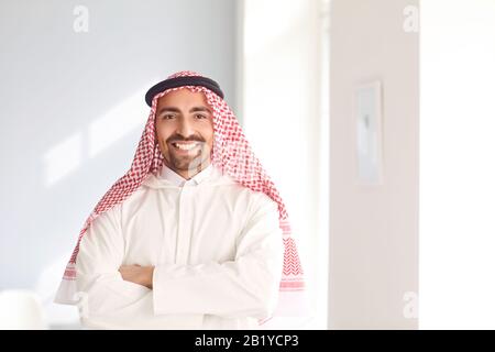 Positiver arabischer Mann lächelt, während er in einem weißen hellen Raum steht Stockfoto