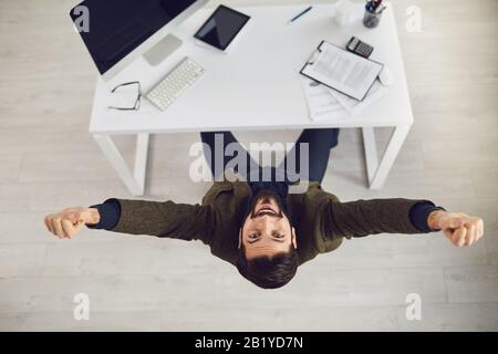 Die Draufsicht eines glücklichen Geschäftsmannes hob seine Hände bei der Arbeit im Büro hoch. Stockfoto