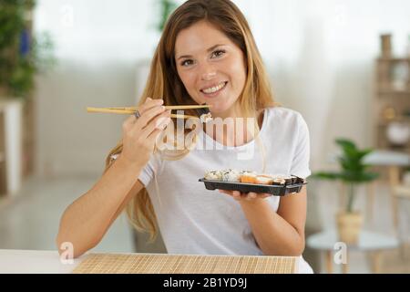 Schöne junge Frau mit Sushi-Rolle zu Hause Stockfoto