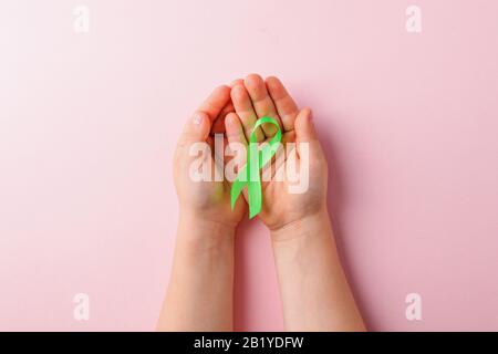 Grünes Satinband, das die Hände der Kinder auf pinkfarbenem Hintergrund hält. Bewusstsein für Leber-, Nierenkrebs, Glaukom-Bewusstsein Stockfoto