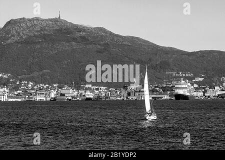 Segelboot Pia II am Byfjorden. Kreuzfahrtschiff Nieuw Statendam, Abfahrt vom Terminal Jekteviken im Hafen von Bergen, Norwegen. Mount Ulriken im Hintergrund Stockfoto