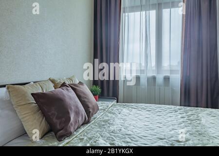 Kopfkissen auf dem Bett und Nachttisch in gemütlichem, bequemem Schlafzimmer in beigefarbenen Farben Stockfoto