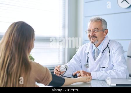 Junge Frau bei Arzttermin. Der Arzt misst den Druck des Patienten Stockfoto