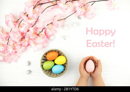 Pastellfarben Eier im Nest mit der Niederlassung der rosa Blumen auf weißem Hintergrund Holz gefärbt. Child's Hände, die rosa Ei auf die Ostern Hintergrund. Stockfoto