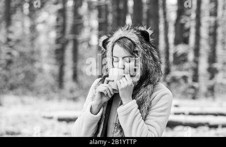 Bester Urlaub. Wärmen Sie sich auf. Frau Winter trinken. Mädchen genießen Glühwein. Frau in Hut trinkt Tee im Wald. Lustige weibliche Pelz-Tiermütze. Wandern und Reisen. Girlhiker trinken Tasse heißen Kaffee. Stockfoto