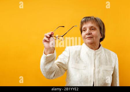 Ältere, reife, charmante Frau blickt in einer Brille auf einem gelben Hintergrund. Stockfoto