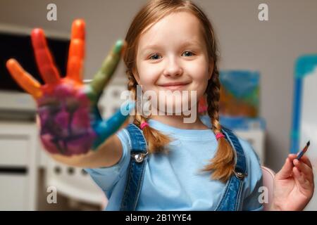 Schöne Mädchen mit Händen in der Farbe. Das Kind zieht am Tisch. Stockfoto
