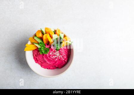 Hausgemachter Rote-Bete-Hummus aus Kichererbsen und Rote Bete in White Bowl mit Karotten- und Gurkenstöcken, hellgrauer Hintergrund. Gesunder Vegetarischer Detox-Snack Stockfoto