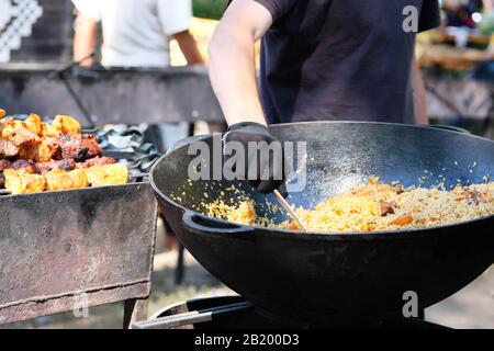 Zubereitung von Pilaf in großem schwarzen Gusseisen mit der Hand des Küchenchefs. Straßenküche und nationale Küche. Stockfoto