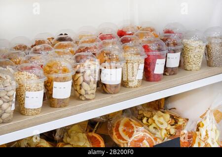 Verschiedene Nüsse und Samen in Plastikbechern: Mandeln, Haselnüsse, Zedernnüsse, Rosinen, Pistazien, Erdnüsse in Regalen auf veganem Markt. Stockfoto