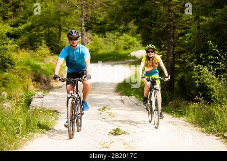 Aktives Junges Paar, das an einem Frühlingstag auf einer Waldstraße in Berg radeln kann Stockfoto
