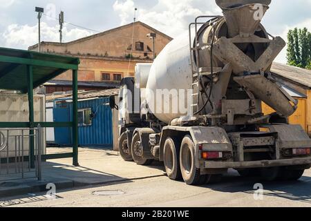 Rückansicht des Zementmischwagens aus schwerem Beton, der mit altem Gebäude auf dem Hintergrund in die Baustelle eindringt. Renovierung oder Wiederaufbau. Stadtentwicklung Stockfoto
