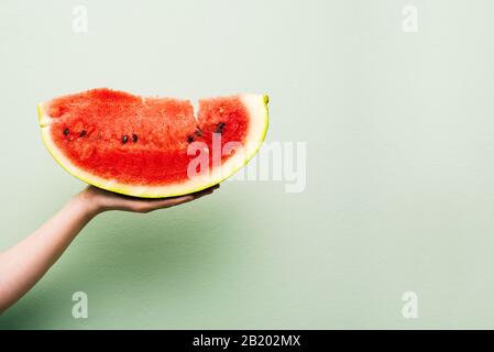 Weibliche Hand hält ein großes Stück Wassermelone. Rote Schicht Wassermelone auf hellgrünem Hintergrund mit Kopierbereich. Sommerkonzept Stockfoto