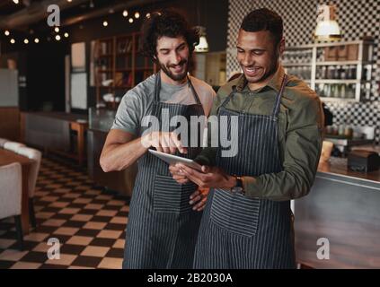 Fröhliche Café-Partner, die in einem Café mit Blick auf den Touchscreen eine Schürze tragen Stockfoto