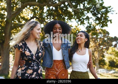 Gruppe lächelnder, fröhlicher multiracial weiblicher Freunde, die an einem sonnigen Tag glücklich im Park zusammen spazieren Stockfoto