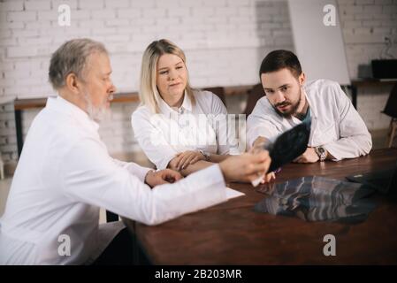 Das dreiköpfige Ärzteteam diskutiert im Beratungsraum eine Röntgenaufnahme eines Patienten. Stockfoto