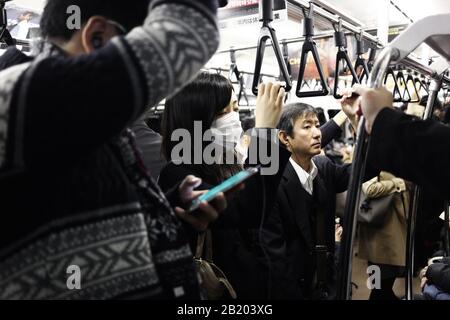 Tokio, Japan - 05. Dezember 2016: Unidentifiziertes Mädchen mit einem Kinnriemen in einem Zug mit anderen Menschen in Tokio, Japan Stockfoto