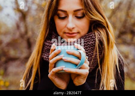 Mädchen trägt Strickpullover und Schal und genießt im Herbst heiße Getränke im Freien. Stockfoto