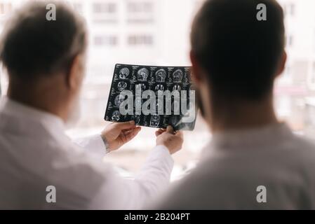 Zwei Ärzte diskutieren die Ergebnisse einer MRT-Untersuchung des Kopfes des Patienten Stockfoto