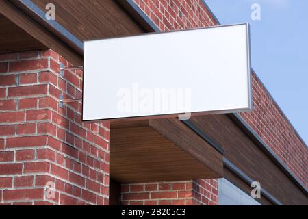Horizontales Singboard oder Beschilderung an der roten Ziegelwand mit leerem, weißem Schild. Ansicht von unten Stockfoto