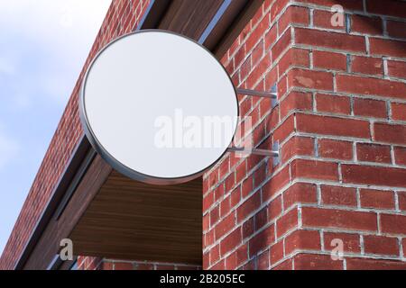 Rundes Singboard oder Schilder an der roten Ziegelwand mit leerem weißem Schild. Ansicht von unten Stockfoto