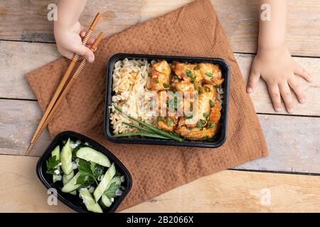 Kinder, die Essstäbchen halten. Asiatische Nudeln mit Broccoli, Bell Pepper, Mushroom und Huhn in Kunststoffboxen, Draufsicht Stockfoto