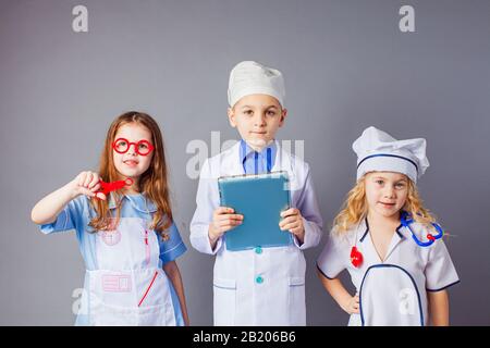 Niedliche kleine Kinder, die sich als Ärzte auf grauem Hintergrund bekleidet haben. Stockfoto