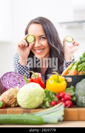 Fröhliche junge Frau, die in der Küche Gurkenscheiben hält - Ernährungskonzept Gemüse und Heide. Stockfoto