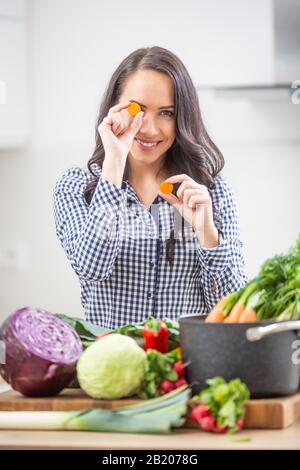 Verspielte junge Frau, die Karotten in der Küche hält - Ernährungskonzept Gemüse und Heide. Stockfoto