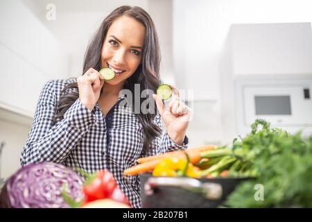 Fröhliche junge Frau, die in der Küche Gurkenscheiben hält - Ernährungskonzept Gemüse und Heide. Stockfoto