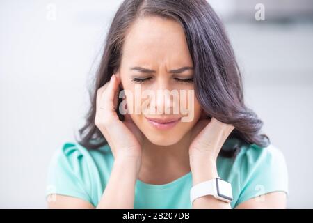 Junge Frau hat Kopfschmerzen Migräne Stress oder Tinnitus - Lärm Pfeifen in ihren Ohren. Stockfoto
