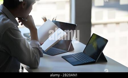 Closeup kreativer Mann, der als Buchhalter arbeitet und Informationen überprüft, während er mit einer Tastaturtasche auf dem Computertablett sitzt, die moderne Arbeitsmittel aufsetzt Stockfoto